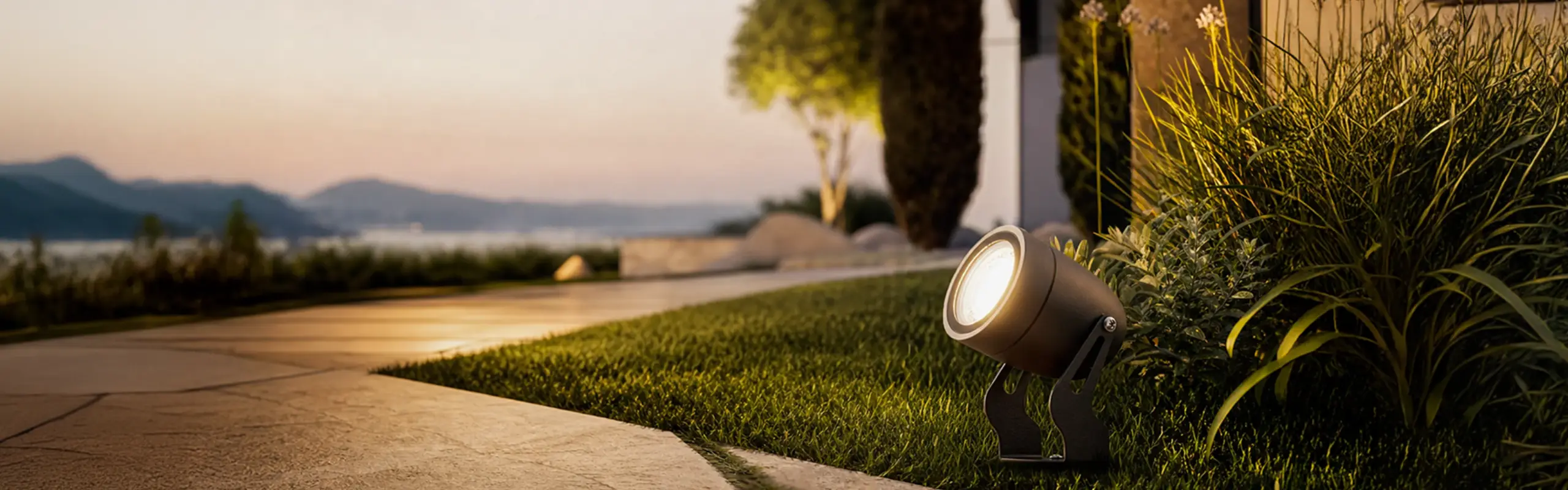 A Fonelight landscape spotlight illuminating garden plants at sunset with a coastal view