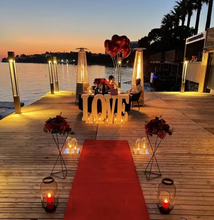 Tall pillar lights framing an outdoor dinner setup on a waterfront deck at sunset